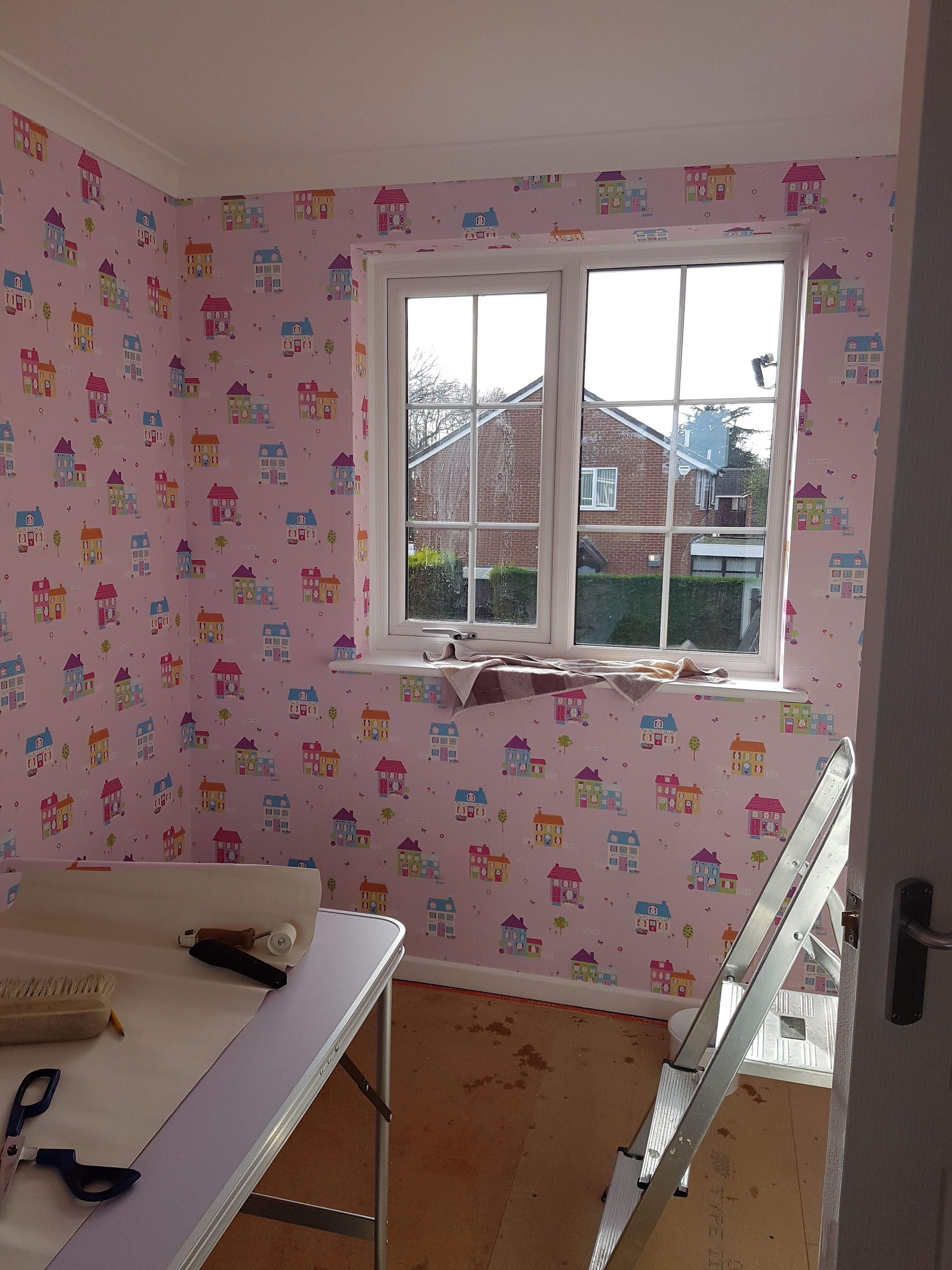 A child’s bedroom mid-way through papering, with the pasting table in the room