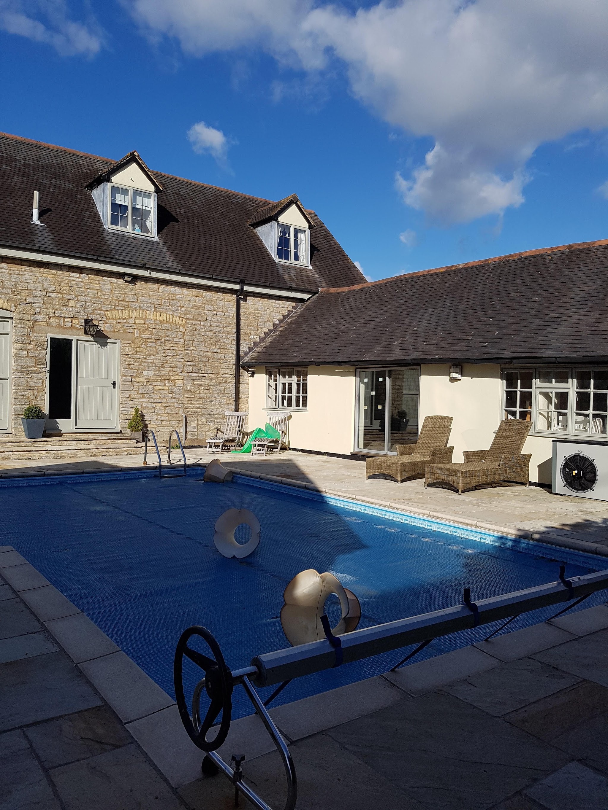 Stone farmhouse with a cream painted wing beside a swimming pool